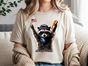 Person wearing a t-shirt with a raccoon graphic holding an American flag and hot dog, sitting on a couch. Person wearing a t-shirt with a raccoon graphic holding an American flag and hot dog, sitting on a couch.