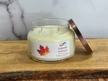 Load image into Gallery viewer, Candle jar labeled 'Autumn Ambrette' with a leaf design on a wooden surface.