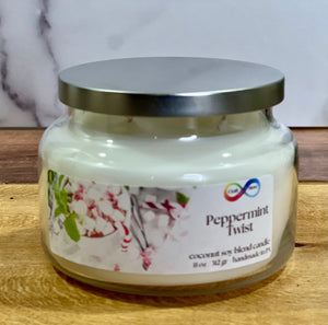 Jar of 'Peppermint Twist' candle with a silver lid on a wooden surface. Jar of 'Peppermint Twist' candle with a silver lid on a wooden surface.