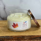 Candle jar labeled 'Autumn Ambrette' with a leaf design on a wooden surface.