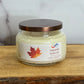 Jar of 'Autumn Ambrette' candle with a maple leaf label on a wooden surface.