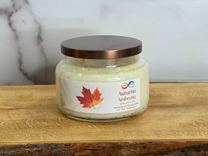 Jar of 'Autumn Ambrette' candle with a maple leaf label on a wooden surface.