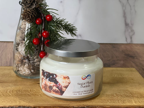 Candle jar labeled 'Sugar Plum Danish' with decorative elements on a wooden surface