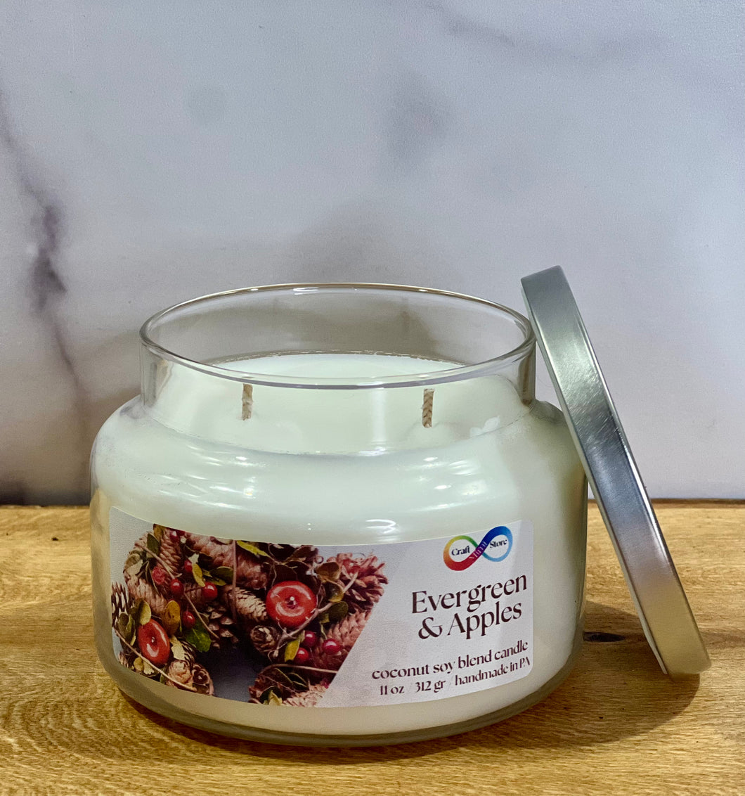 Candle jar labeled 'Evergreen & Apples' on a wooden surface with a marble background