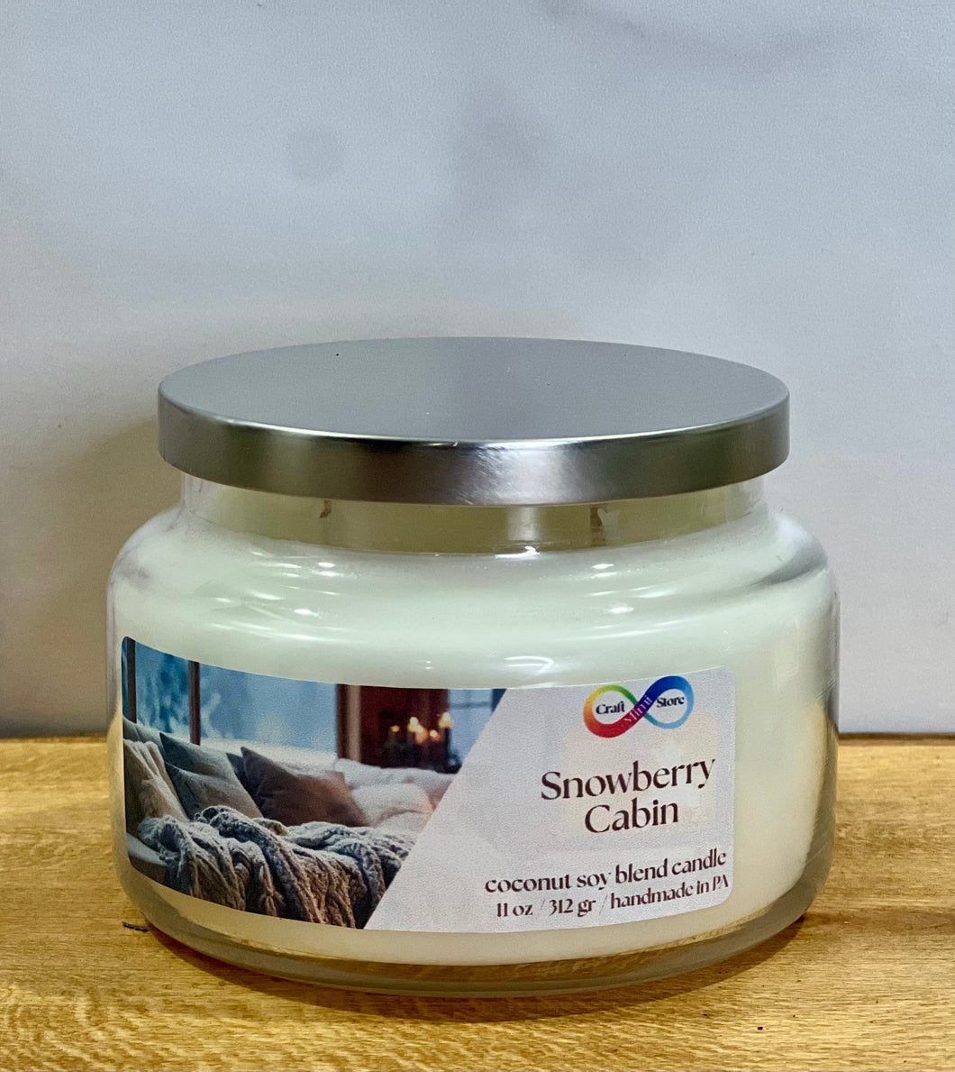 Jar candle labeled 'Snowberry Cabin' on a wooden surface with a white background