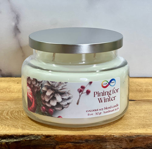 Candle jar labeled 'Pining for Winter' on a wooden surface with a neutral background