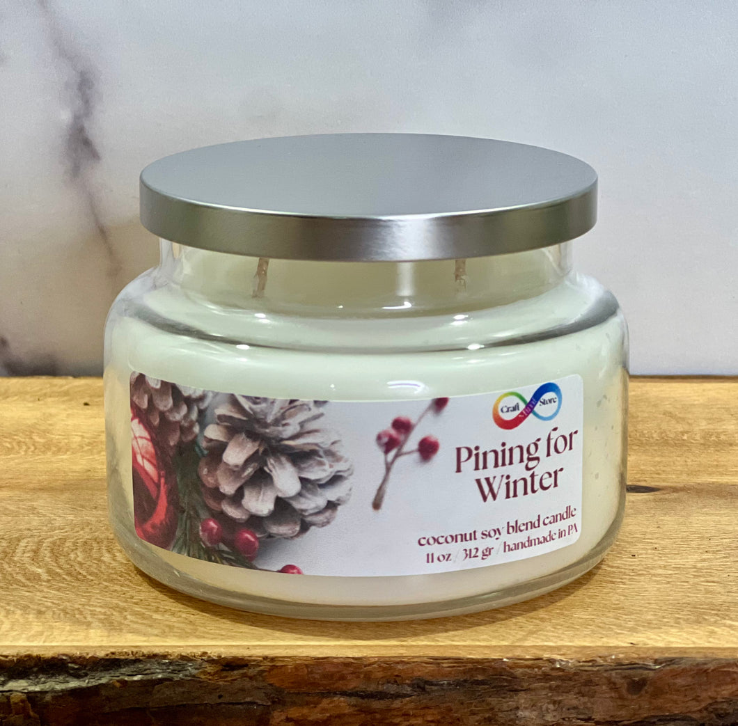 Candle jar labeled 'Pining for Winter' on a wooden surface with a neutral background