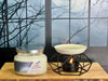 Candle labeled 'Dark Orchard' and a ceramic oil burner with a lit candle on a wooden surface.