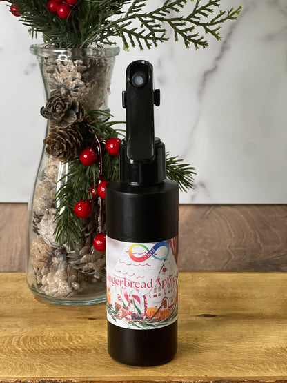 Spray bottle with gingerbread apple label next to a decorative vase with greenery and berries on a wooden surface.