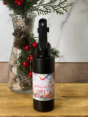 Spray bottle with gingerbread apple label next to a decorative vase with greenery and berries on a wooden surface.