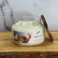 Candle jar labeled 'Harvest' on a wooden surface with a marble background