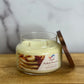 Jar candle labeled 'Maple Walnut Pancake' on a wooden surface with a marble background